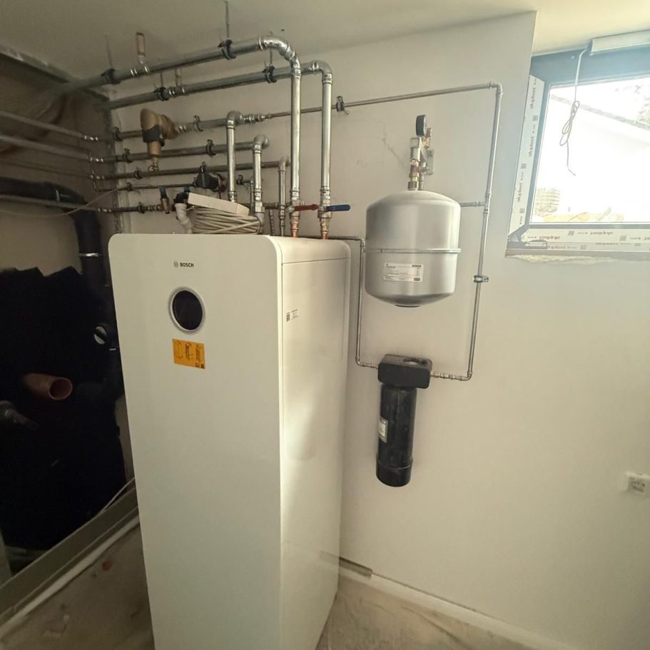 Eine kompakte Luft-Wasser-Wärmepumpe im Betrieb während des Berliner Winters, leicht mit Schnee bedeckt vor einer modernen Hausfassade.