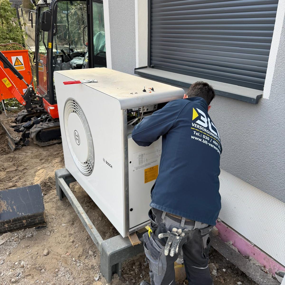 Eine moderne, graue Luft-Wasser-Wärmepumpe steht im gepflasterten Innenhof eines sanierten Berliner Altbaus mit charakteristischer Stuckfass